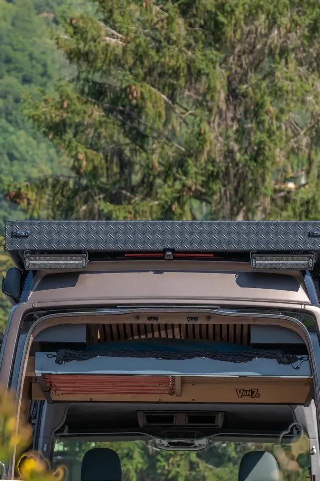 Ein Blick in den VW Crafter 4x4 mit geöffneten Hecktüren. Der Camper Van von Cocoon Vans verfügt über ein Hubbett, der Innenausbau ist aus amerikanischem Nussbaum gefertigt.