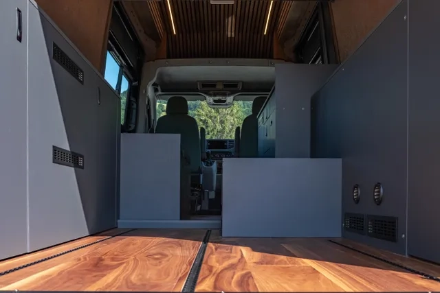 Der Boden der Garage vom Camper Van von Cocoon ist aus amerikanischem Nussbaum. In den Boden sind Airline Schienen für die Ladesicherung eingelassen. Seitlich sind graue Möbel eingebaut, in denen die ganze Technik verstaut ist.