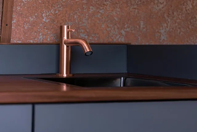 Bronzefarbener Wasserhan. Hat fast die gleiche Farbe wie die Wandbeplankung aus Leichtbauplatte Rostimitat. Die Arbeitsplatte im Camper Van von Cocoon Vans ist aus amerikanischem Nussbaum die Fronten sind dunkelgrau lackiert.