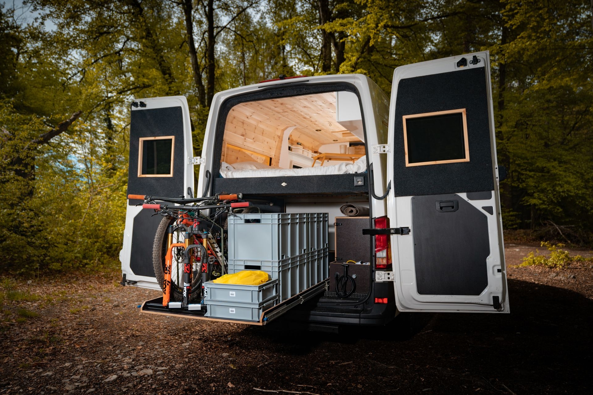 Geöffnete Hecklappen, gefilzte Türen unter dem Bett eine Garage mit 2 Bikes, Schwerlasauszügen und einer Camper Van Dusche