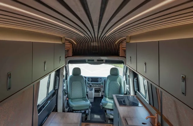 Innenausbau von Cocoon Vans eines VW Crafters 4x4 mit Holzakzenten aus amerikanischem Nussbraum, zwei grünen Ledersitzen, viel Stauraum über Kopf und einem kompakten Küchenbereich.