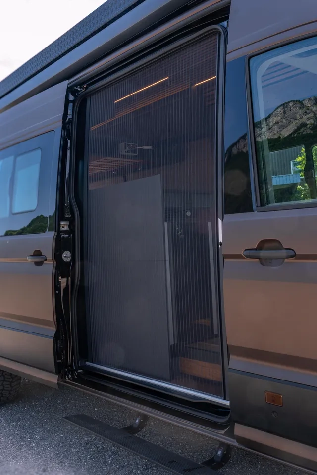 Ausfahrbare Tritt für den Einstieg in den VW Crafter 4x4. Das Fliegengitter an der Seitentür ist geschlossen.