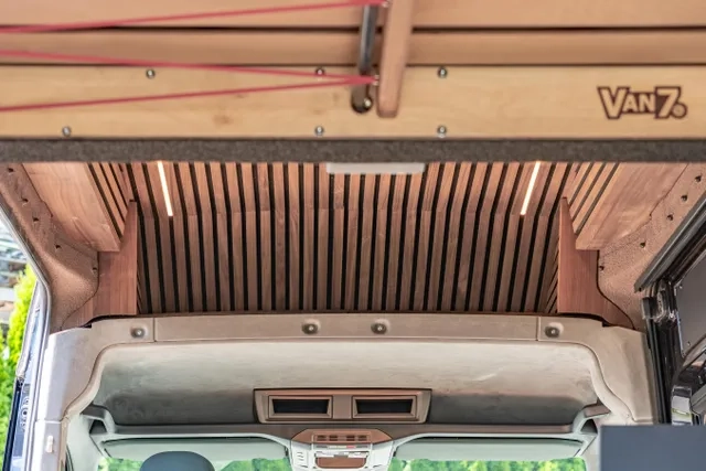 Blick vom Heck in den Bereich oberhalb der Autositze. Die Decke ist aus amerikanischem Nussbaum, beide seitentüren sind geöffnet und von hellbraun Sprükork eingerahmt. Der Ausbau wurde von Cocoon Vans umgesetzt.